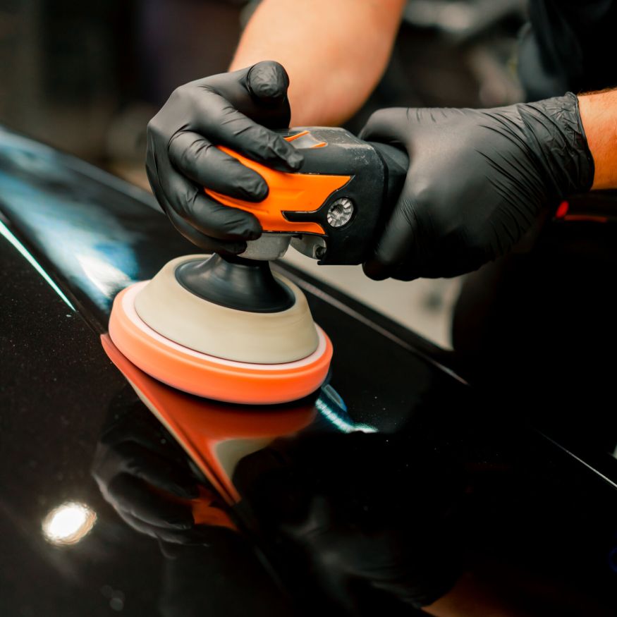 Close-up of a car wash worker using a polishing machine to polish the hood of black luxury car Close-up of a car wash worker using a polishing machine to polish the hood of black luxury car